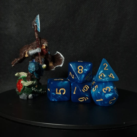 Blue polyhedral dice set with gold numbers on a black surface against a dark background