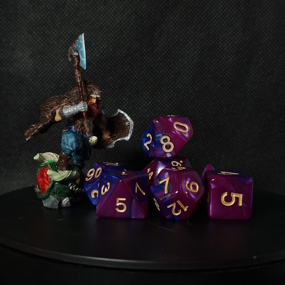 Set of purple polyhedral dice with gold numbers on a black surface.
