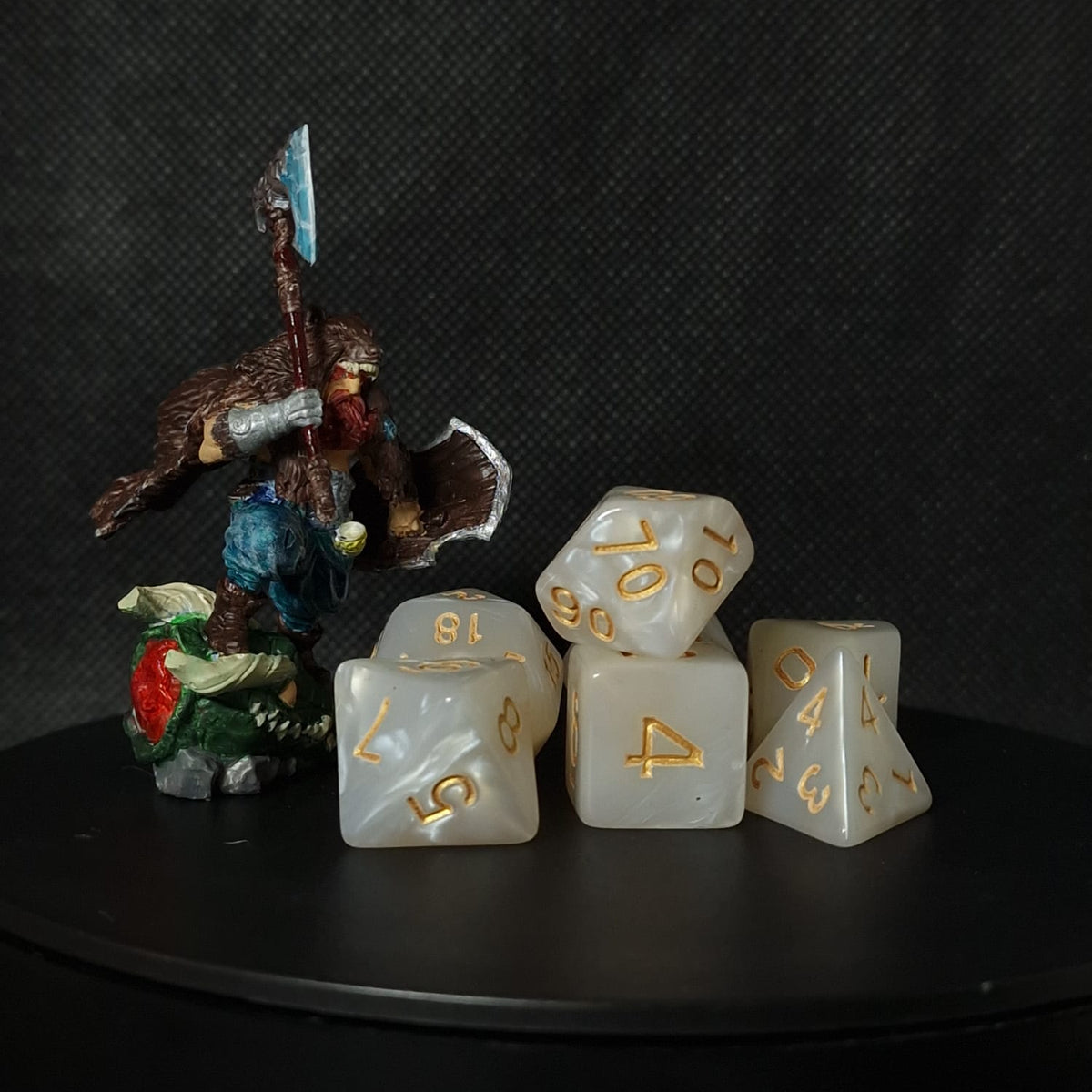 Set of white polyhedral dice with gold numbering on a black surface.