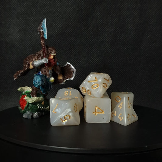 Set of white polyhedral dice with gold numbering on a black surface.