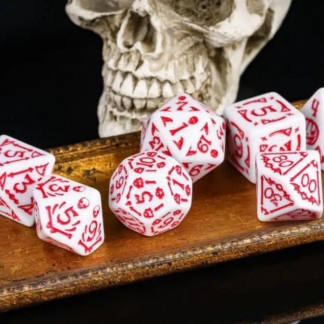 White dice with red numbers on a wooden surface in front of a skull.