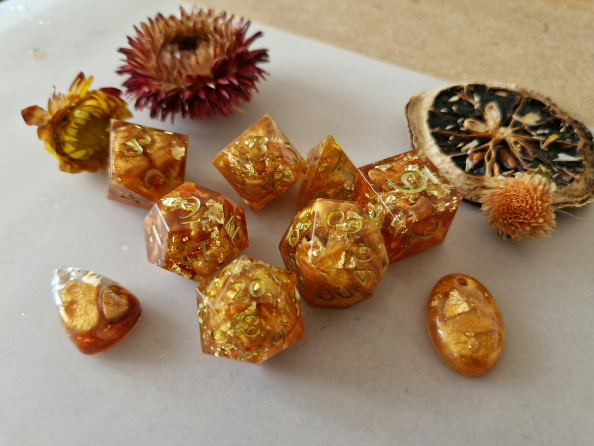 Fallen Leaves epoxy resin dice set with amber-orange swirls, gold-coloured flakes and golden numbers.