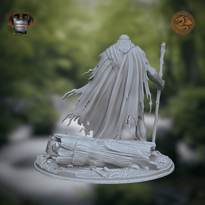 A light gray unpainted fantasy miniature figurine featuring a romanian folklore character - Ochila - a bearded warrior holding a staff, standing on a detailed rocky base. The background is a blurred green forest scene.